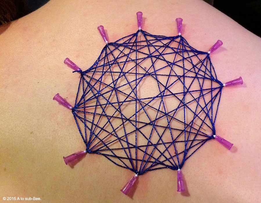 A close up of Bee's back showing their first experience of needle play with a geometric shape strung between them.
