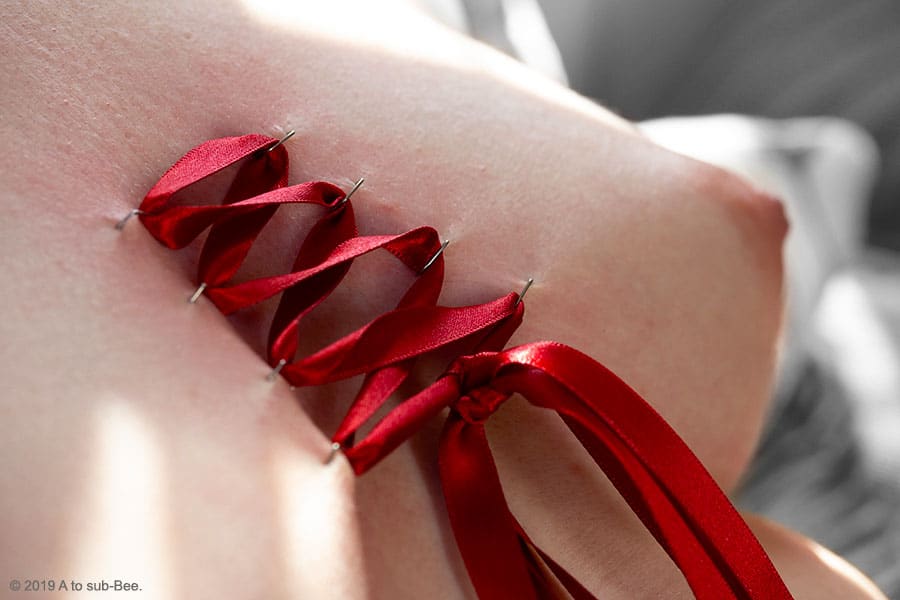 Bee's breasts stapled and tied together with red ribbon