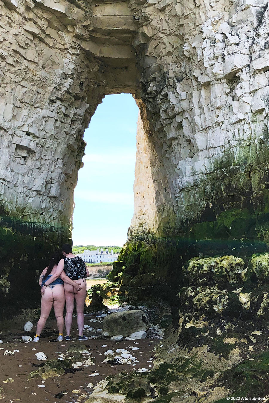 Bee & Honey stand under a huge coastal arch flashing their bottoms