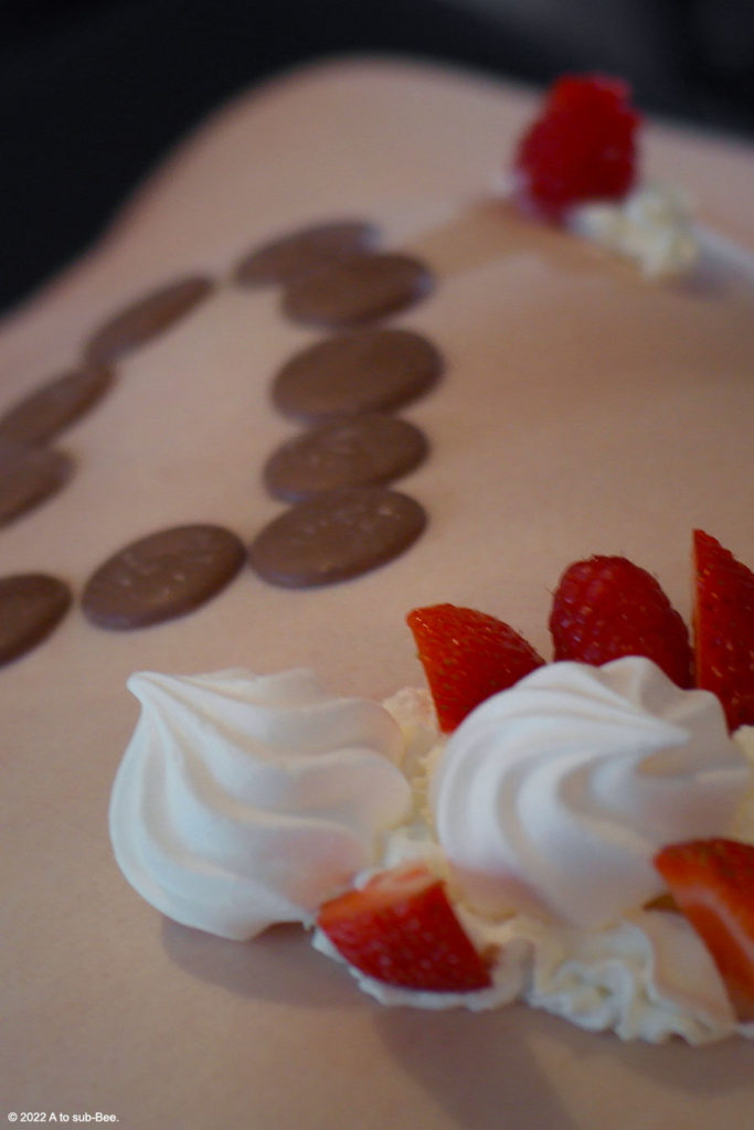 Bee's naked body with a heart made from chocolate buttons, cream and fruit laid out as a platter