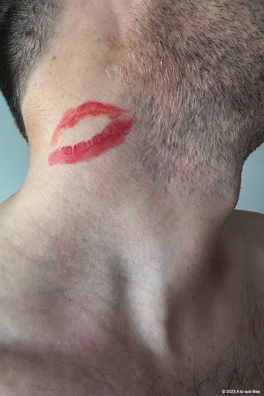 A man's neck with him looking up and to the tight. His salt and pepper stubble looks so hot as does the bright red lipstick mark that's been left behind