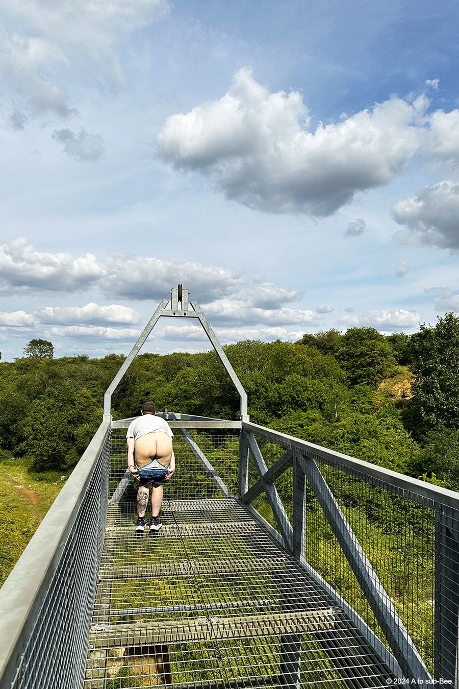 A long plaform across a quarry with a person bending over at the end exposing their bare arse