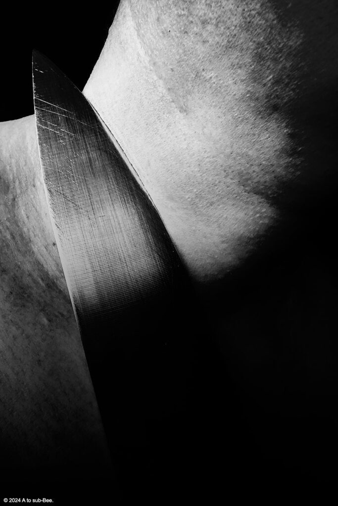 A dark black and white image of a sharp knife being held aganinst a persons throat