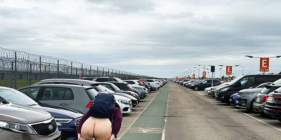 Image of a person bending over and exposing their arse in a big airport car park