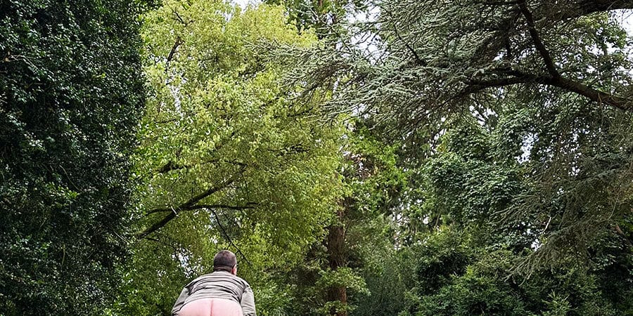 A person bent over bearing their bottom whilst being surrounded by trees in an arboretum